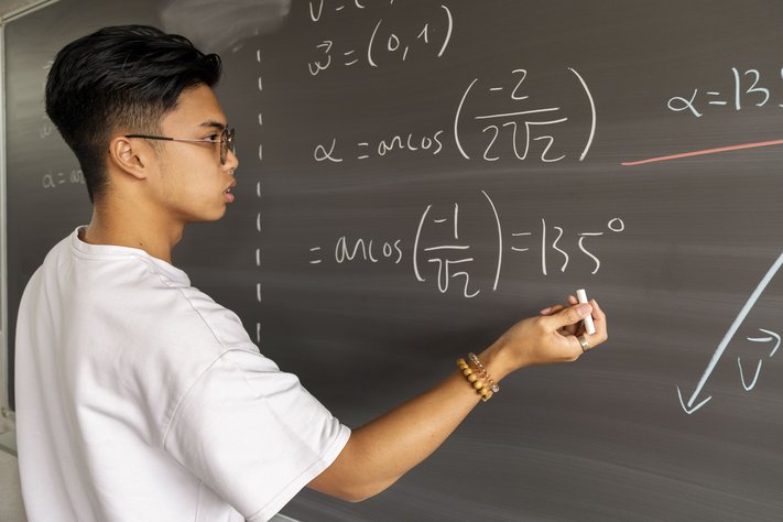 A young asian man completes maths equations on a chalkboard.