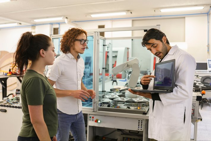 A male scientist shows laptops to junior scientists in robotics laboratory.