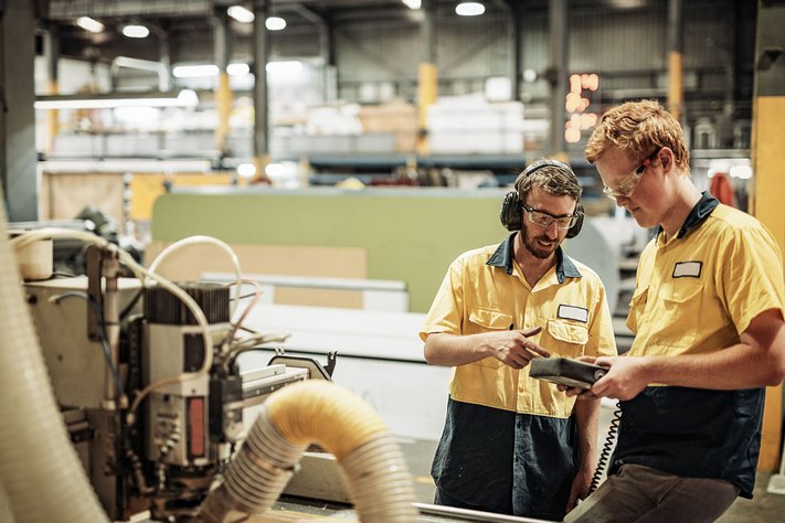Two engineers analyse a reading from a machine. They are in a large warehouse.