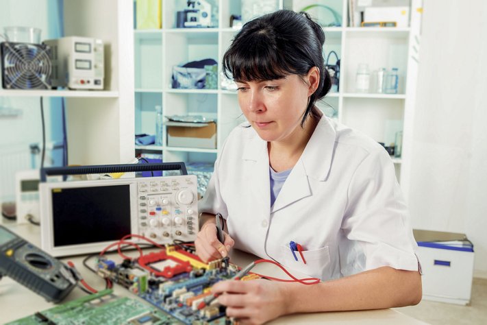 A young woman repairs a circuit board in a laboratory.