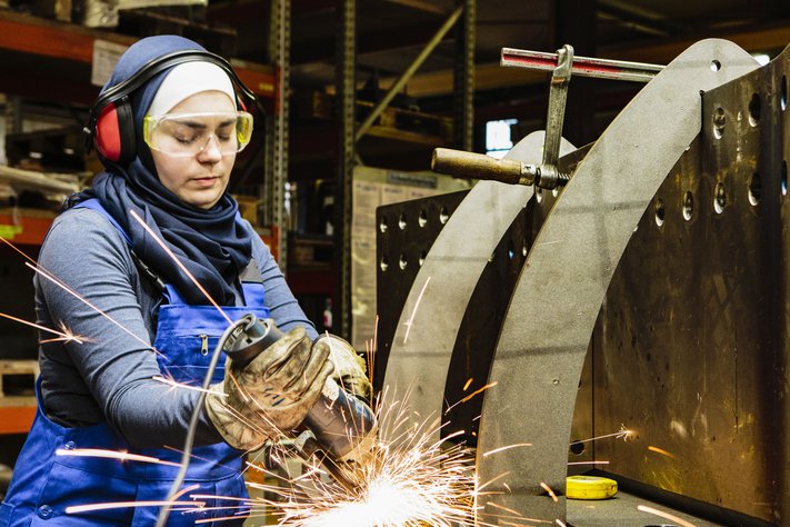 An aerospace engineer in protective equipment welds metal.