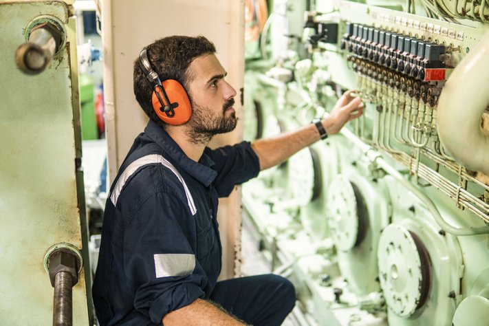 A marine engineer turns a valve in the engine control room.