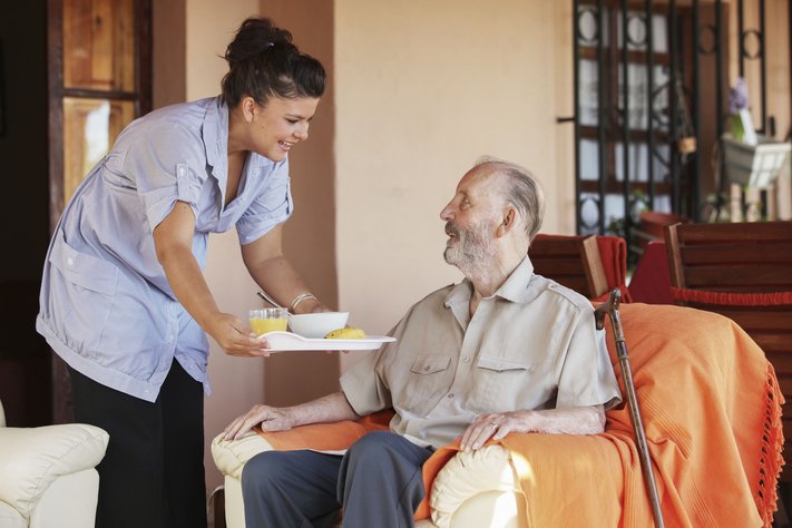 A young nurse provides elderly man with breakfast.