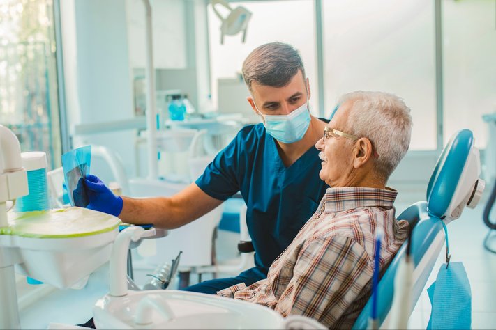 A young male dentist shows sheet to senior male patient.