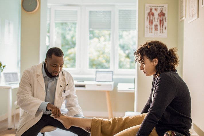 A male podiatrist inspects a female patient's foot.