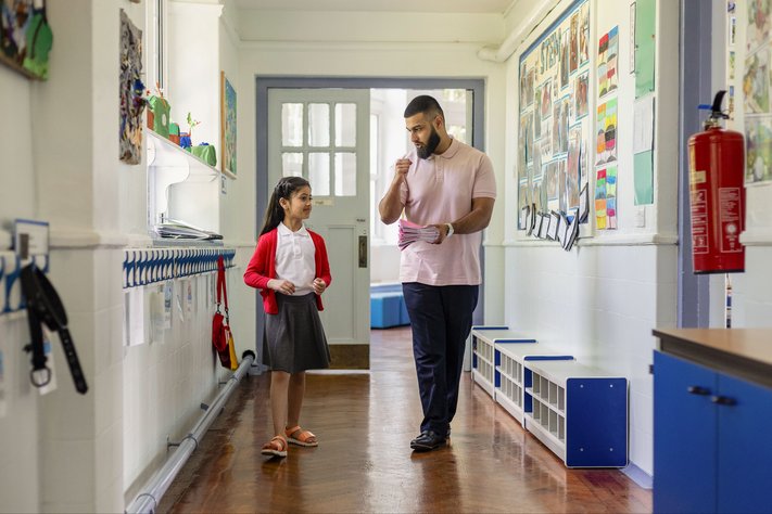 A male teacher discusses with female student in the corridor.