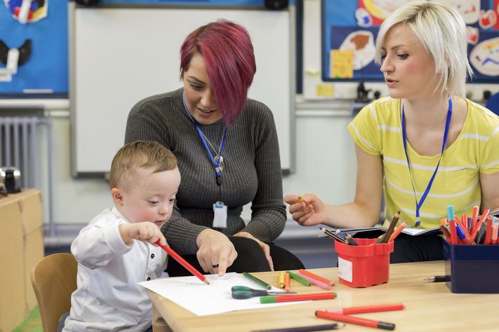 A nursery teacher sits with a parent and her Down Syndrome son in the classroom.