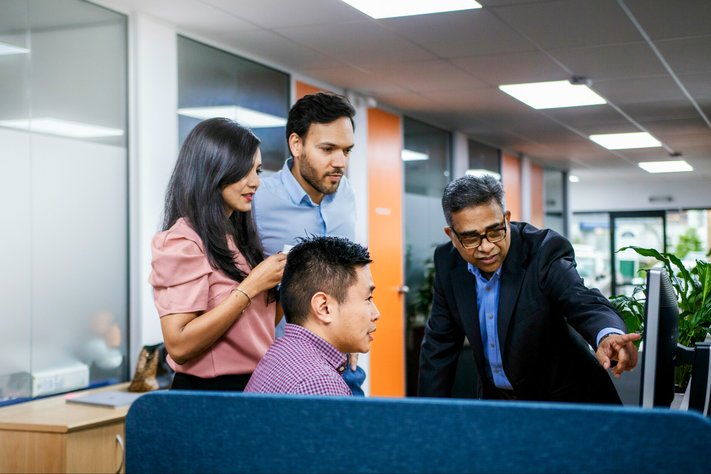 Group of Asian business people view computer in office.