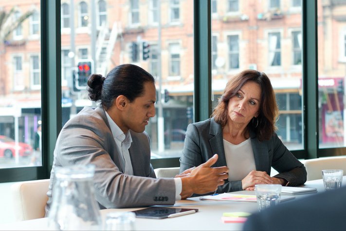 A male businessman and female businessman discuss in modern boardroom.