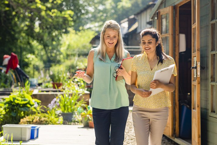 Two female professionals discuss in a sunny outdoor space.