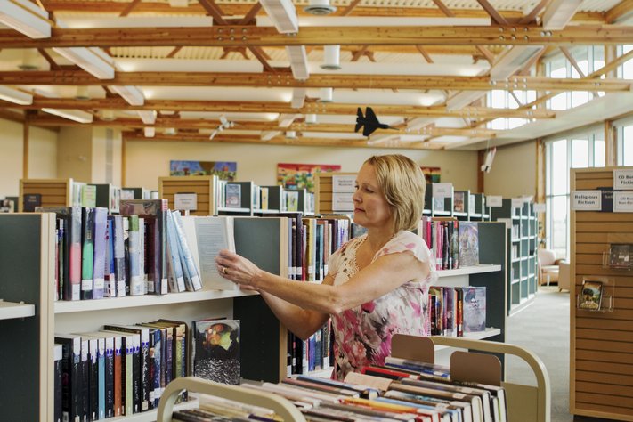 A female librarian places books in bookshelf.
