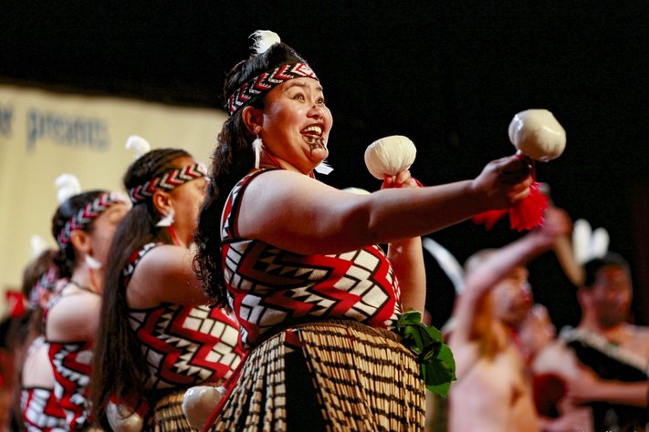 A woman holding poi performs kapa haka. She is adorned in Māori cultural dress.