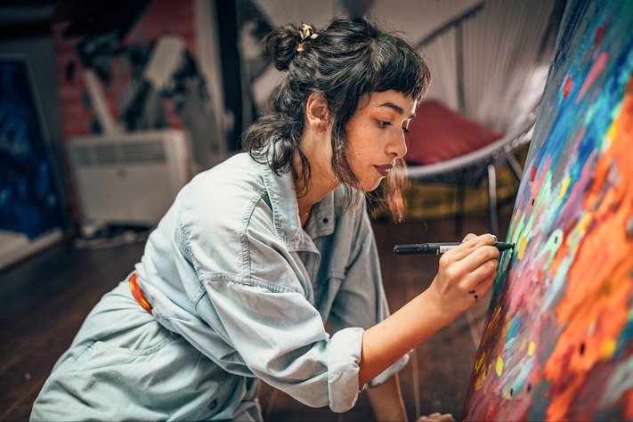 A young female artist draws on canvas in studio.