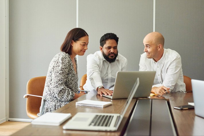 A group of professionals view laptop in boardroom.