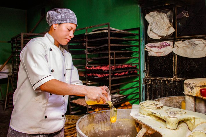 A young baker adds eggs into a large dough mixer.