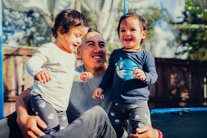 A man plays with his two children on trampoline.