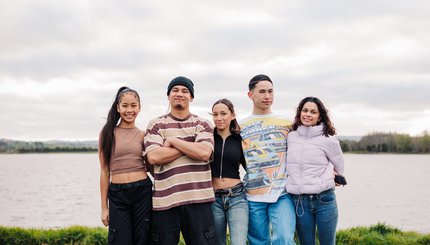 5 teenagers stand by the water looking at the camera.