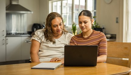 A mother and daughter look at a laptop on their kitchen table.