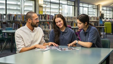 A man sits at a table with 2 students discussing images