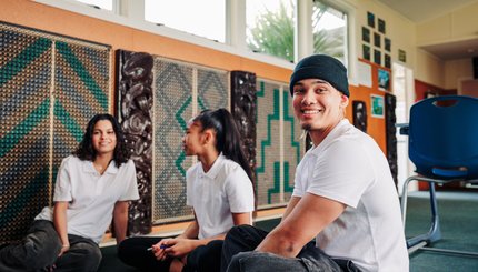 Three students sit on the floor of a classroom.