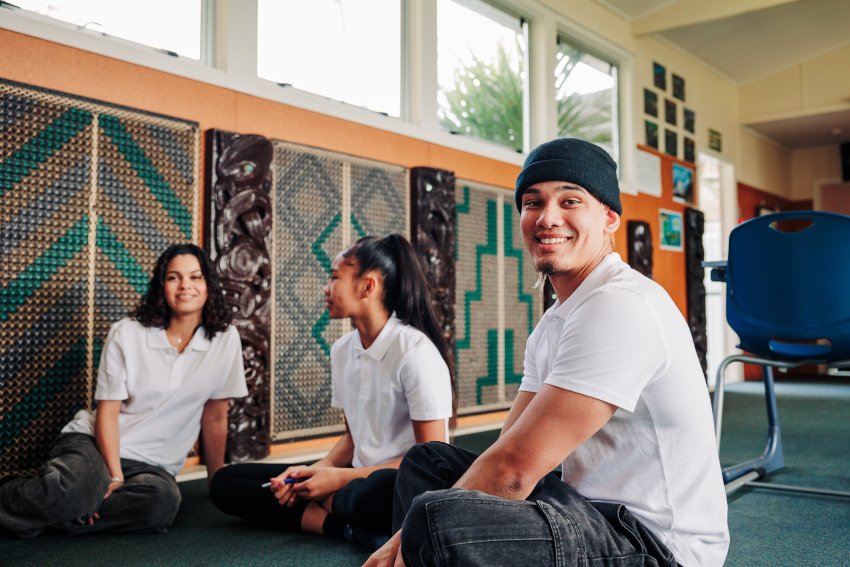 Three students sit on the floor of a classroom.