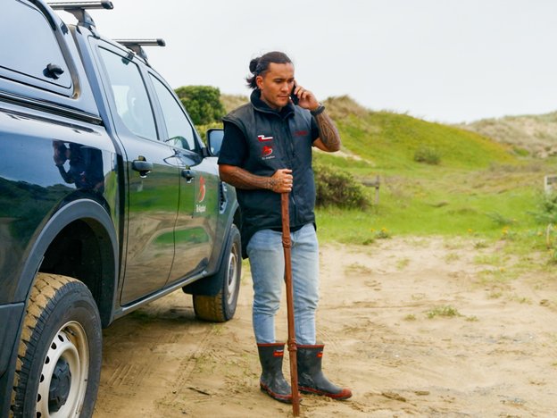 Kei te tū tētahi tangata i te taha o tētahi waka whakahuri wīra-4 e pātata ana ki ētahi tāhuahua kirikiri e kōrero ana i tētahi waea pūkoro.