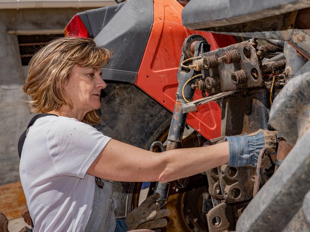 A woman wearing gardening gloves inspects agricultural equipment.