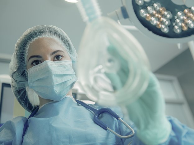 A female medical professional holds an anaesthetic mask. She is in an operating room.