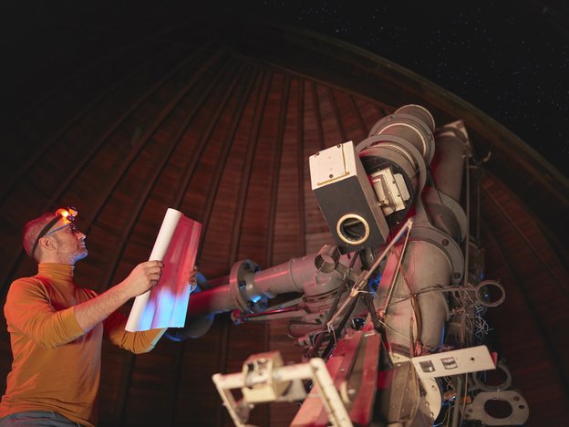 A man holds a document as he looks at spectroscope. He wears a head torch.