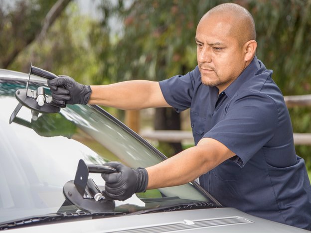 A person places new windscreen onto car. They are using suction clamps to hold the windscreen.