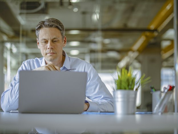 A man looks at an open laptop. He sits at a desk in an office.