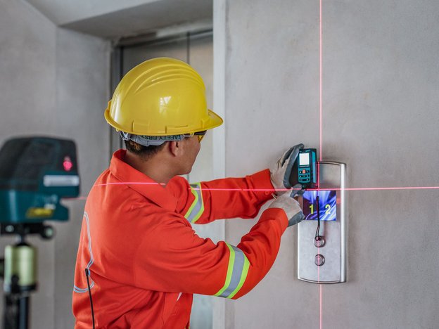 A man is performing tests on a lift. He wears a jacket with yellow and silver stripes and a yellow helmet.