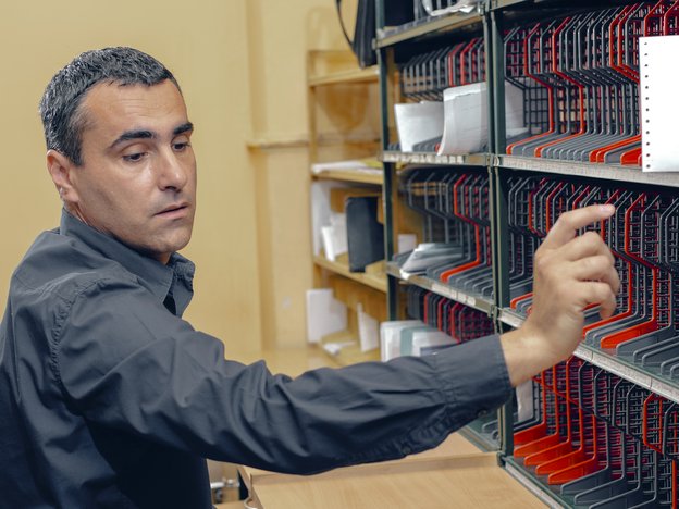 A mail clerk searches mail slots. Some documents and letters can be seen in the mail slots.