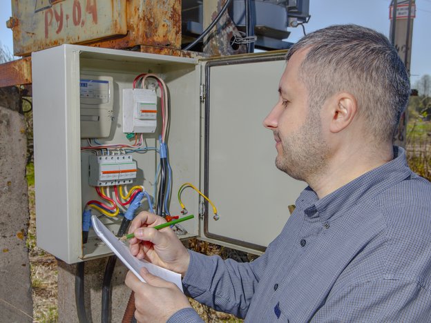A man reads a meter outside. He writes notes on a piece of paper.