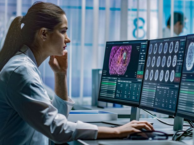 A female neurologist looks at computer monitors. Scans of the brain are displayed on the screen.