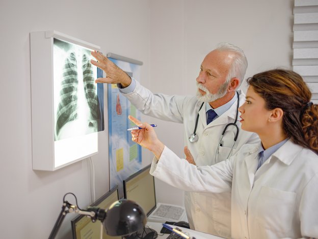 Two medical professionals observe an x-ray scan. They are wearing white lab coats.