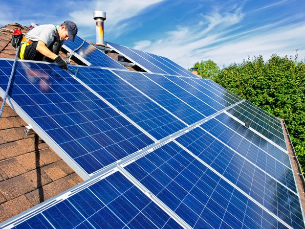A man installs solar panels on to a roof of a house.