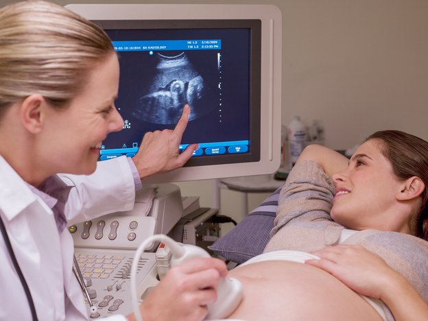 A female sonographer does an ultrasound scan on a pregnant patient. The patient is looking at their sonogram while the sonographer points to it on the screen.