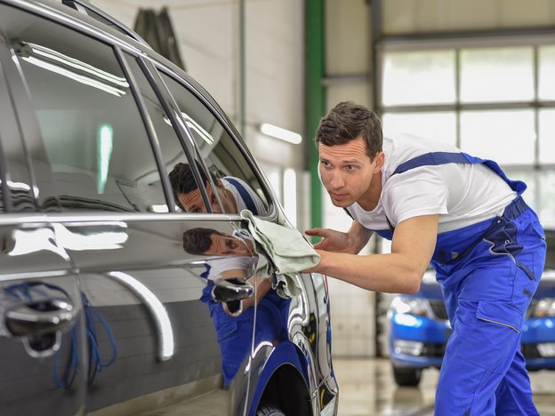 A man in blue overalls and a white t-shirt cleans a black car.