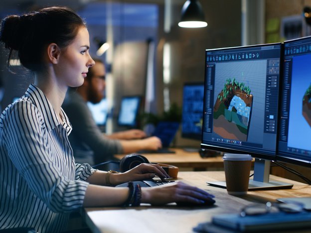 A video game developer designs a level using computer software. They are in a dimly lit office.