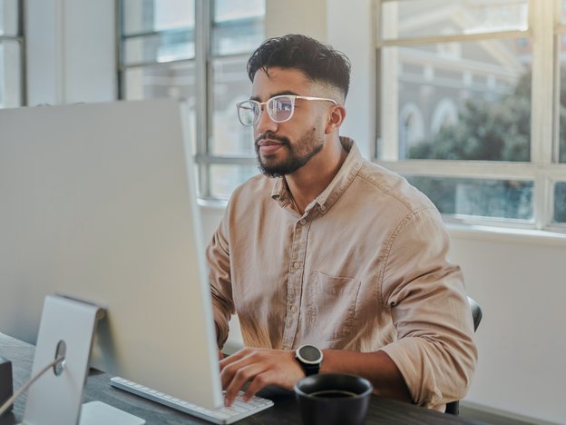 A man is focused on a computer sitting at a desk.