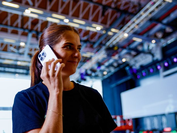 A person takes call on their phone. They are indoors, within a large backstage area.