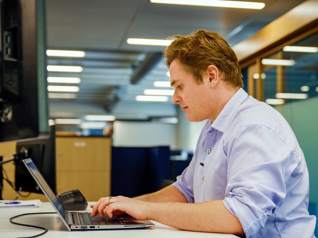 Man sitting at a desk in an office typing on a laptop