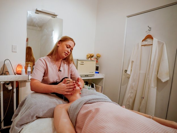 A beauty therapist is giving a client a face massage using their hands. The client is lying down.