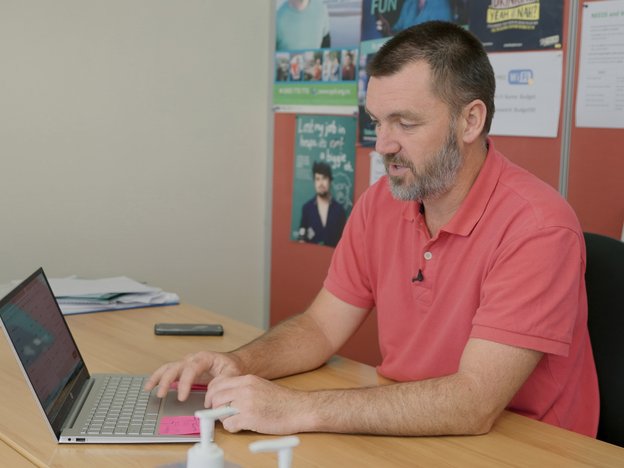 A man sits at a desk and uses a laptop.