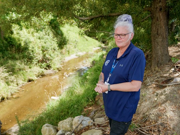 A woman wearing a lanyard stands on a path next to a river.