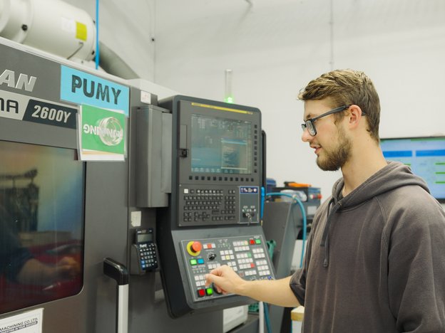 A person uses a CNC machine. They are pressing a button while watching the creation process.