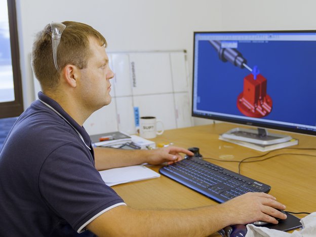 A male looks at a computer screen and sits at a desk.