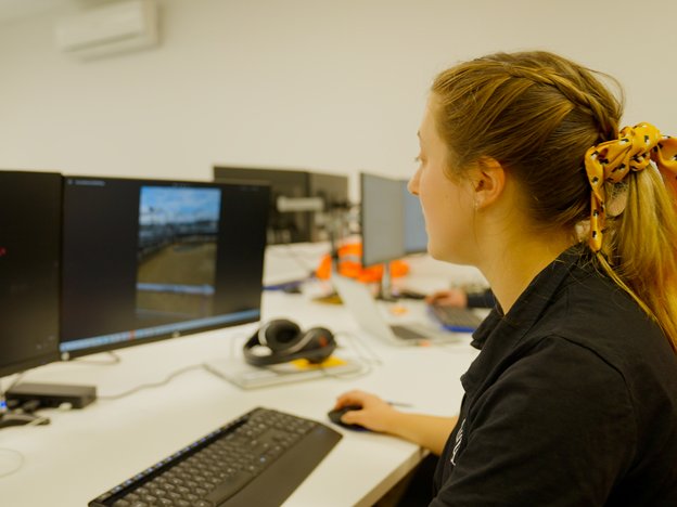 An person views an image on a computer at their work desk. They are wearing a black shirt and have a yellow hair tie.