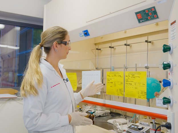 A woman looks at records in a laboratory. She is wearing a white lab coat.